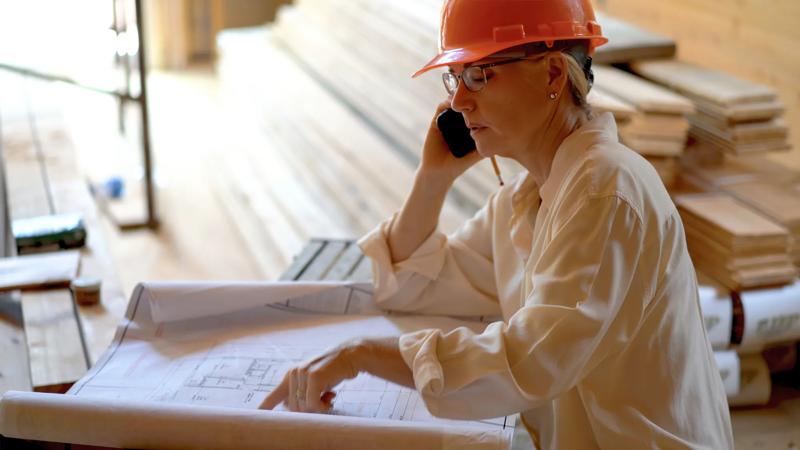Profile shot of woman mechanical engineer on phone discussing and reviewing blueprints on a new construction job site.